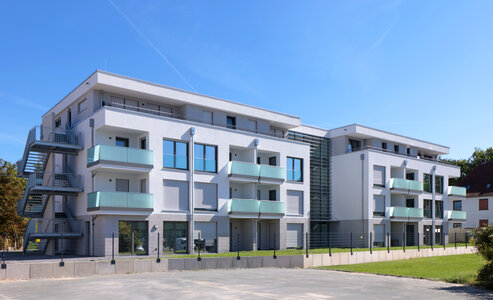 Weißes dreigeschossiges Mehrfamilienhaus mit Staffelgeschoss vor einem blauen Himmel