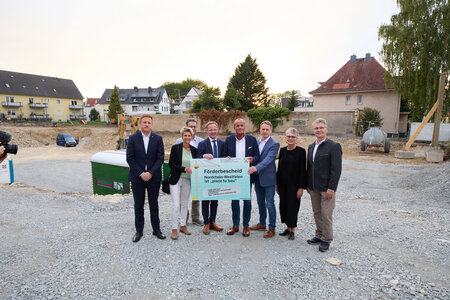 Sieben Personen, zwei Frauen fünf Männer, stehen auf einer Baustelle. Zwei Männer davon halten mittig ein Plakat.
