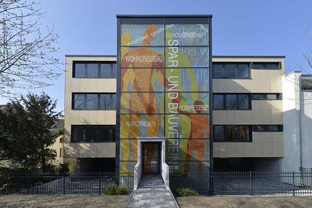 Viergeschossiges Gebäude mit großem bunten Glastreppenhaus vor einem blauen Himmel in der Winterzeit
