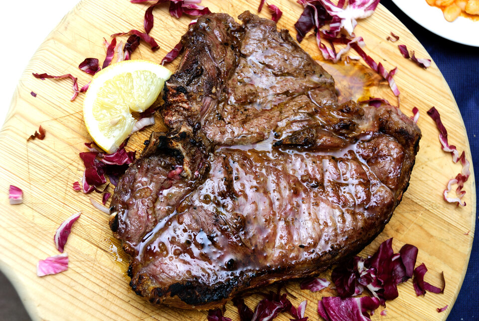 Ein gerilltes Steak auf einem Holzteller angerichtet mit einer kleinen Zitronenscheibe