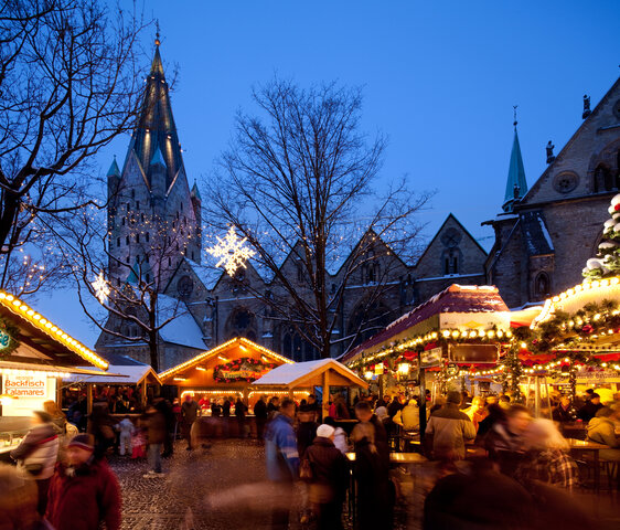 Bunt beleuchtete Weihnachtsstände vor dem Paderborner Dom im Licht der Dämmerung.