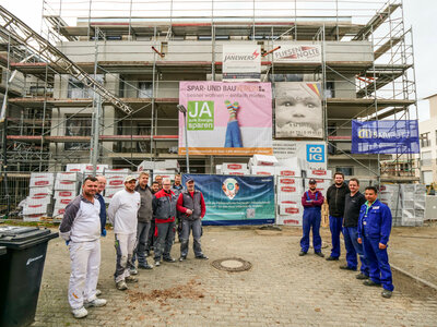 Handwerker verschiedener Gewerke stehen vor einer Baustelle