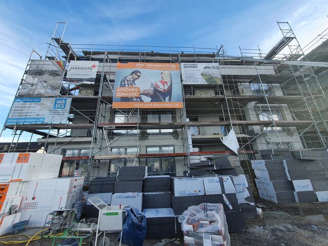 Fassade eines Neubaus mit vielen Baustellenplakaten vor blauem Himmel