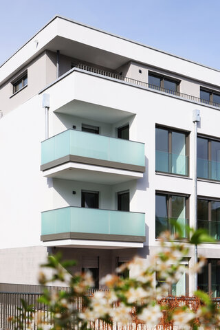 Viergeschossiges weißes Gebäude mit 2 Balkonen und Glasbrüstung darüber eine Penthousewohnung.