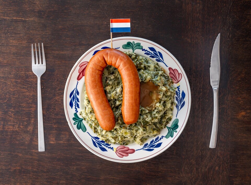 Ein bunter Porzellanteller auf dem Grünkohl und einer halbrunde Wurst mit einem niederländischen Stickerfähnchen