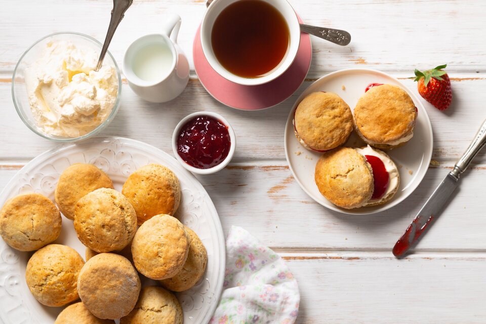 Frühstückstisch mit Brötchen auf einem weißen Teller, Marmelade, eine Tasse Tee