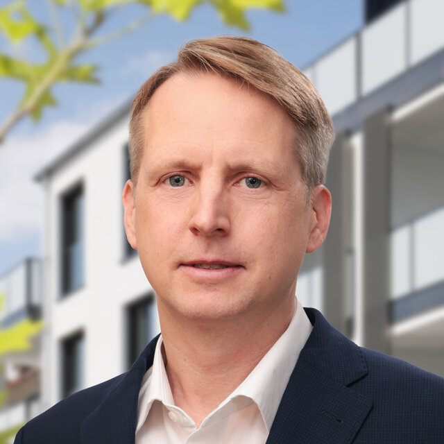 Prokurist Alexander Prior in weißem Hemd mit blauem Sakko vor einem Haus.