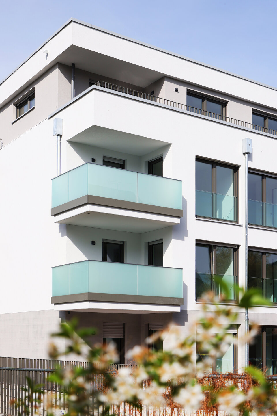 Viergeschossiges weißes Gebäude mit 2 Balkonen und Glasbrüstung darüber eine Penthousewohnung.