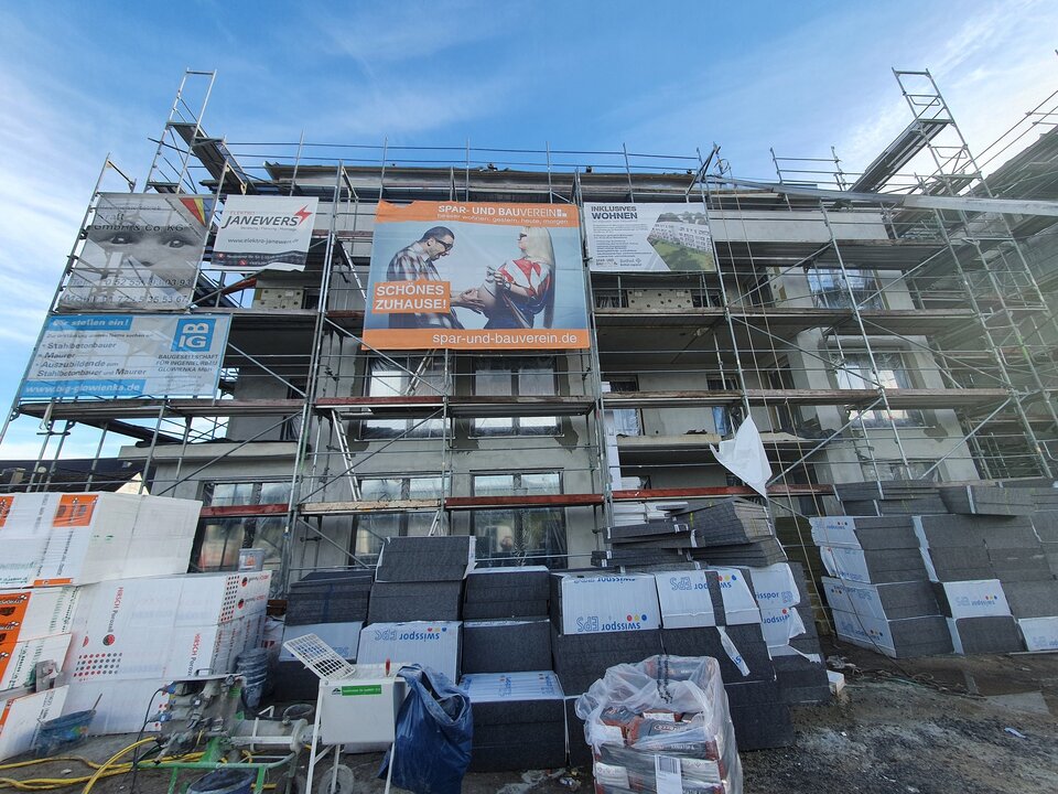Fassade eines Neubaus mit vielen Baustellenplakaten vor blauem Himmel