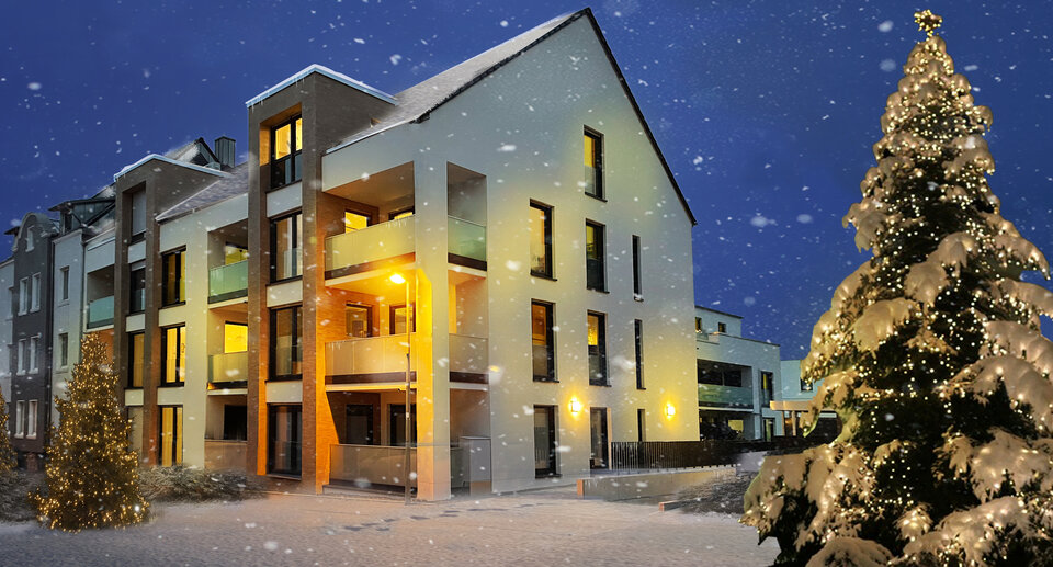 Mehrfamilienhaus in der Dämmerung weihnachtlich beleuchtet mit verschneitem Weihnachtsbaum