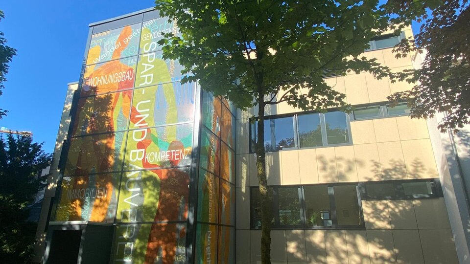 Buntes Treppenhaus an einem dreistöckigen Gebäude vor einem blauen Himmel und grünen Bäumen