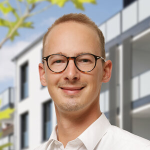 René Reuner vor einem modernen Gebäude blickt lächelnd nach in die Kamera.