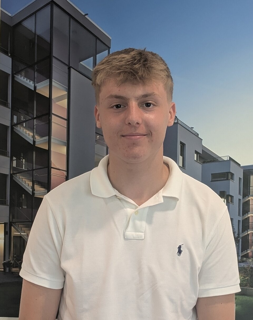 Junger Mann in einem weißen Polo-Shirt vor einem beleuchteten mehrstöckigen Haus