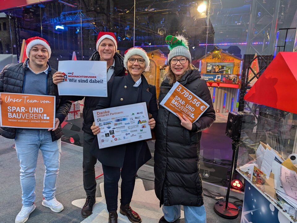Vier Personen, zwei Männer, zwei Frauen und weihnachtlicher Kopfbedeckung mit Schildern in der Hand.