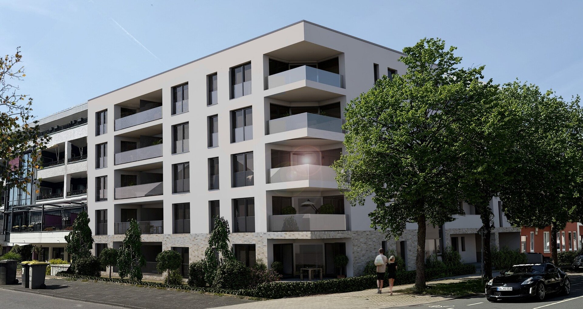 Ein modernes, weißes Mehrfamilienhaus mit Balkonen und einem Flachdach steht an einer Straßenecke, umgeben von Bäumen und einem schwarzen Auto.