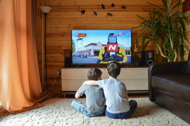 Zwei Kinder sitzen Arm in Arm vor einem Fernsehgerät